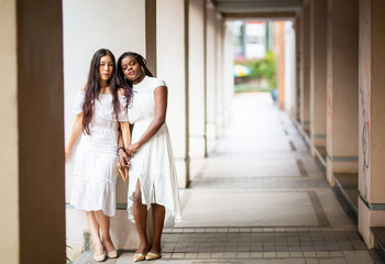 Fototapeta premium portrait of Asian and African american women in white dress against street