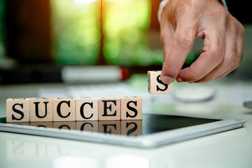 Close up hand holding wooden cube with SUCESS word on table, business conceptual, sucess in business concept