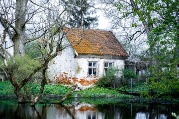 Old German-style house with a tiled roof. It stands on the shore of the lake. It is covered with ivy and wild grapes.