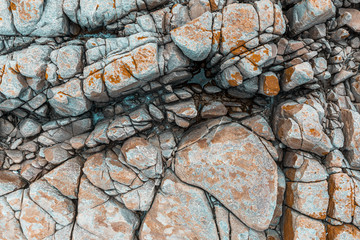 Surface of grey stones with cracks, water & orange moss spots in between.