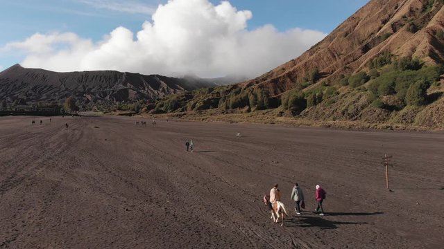 Aerial shot of Mount Bromo's Sea of Sand, morning light, flyover tourists walking and horseriding to Bromo. Java, Indonesia