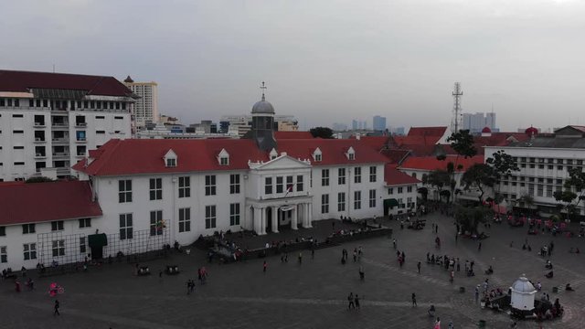 Aerial shot, flying backwards, of Dutch colonial City Hall building in Jakarta, Java Indonesia. Tourists cycling on public Taman Fatahilah square in front of city hall.