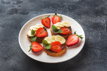 Delicious sandwiches with chocolate nougat, strawberry and banana. Concept of Breakfast. Dark concrete background.