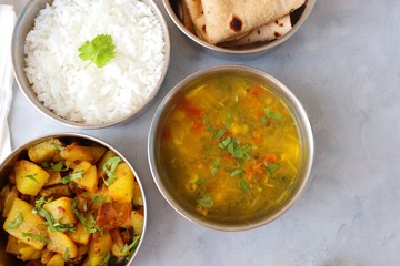 Stainless steel Lunch Box or Tiffin with Indian food menu Chapati or Roti, Garlic Dal Tadka, White Rice and Potato or Jeera aloo. with spoons, tissue paper and glass of water. Copy space