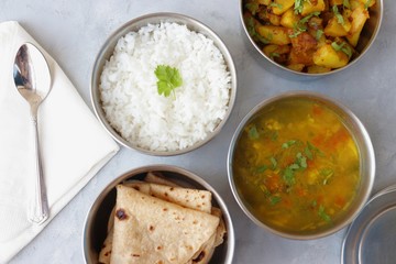 Stainless steel Lunch Box or Tiffin with Indian food menu Chapati or Roti, Garlic Dal Tadka, White Rice and Potato or Jeera aloo. with spoons, tissue paper and glass of water. Copy space