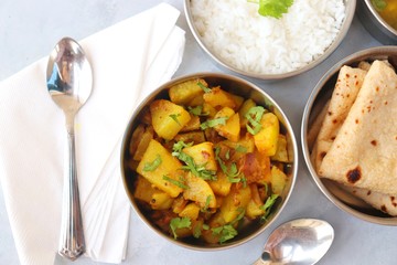 Stainless steel Lunch Box or Tiffin with Indian food menu Chapati or Roti, Garlic Dal Tadka, White Rice and Potato or Jeera aloo. with spoons, tissue paper and glass of water. Copy space