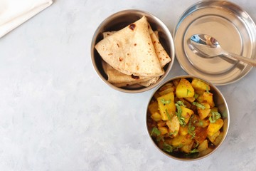 Stainless steel Lunch Box or Tiffin with Indian food menu Chapati or Roti, Garlic Dal Tadka, White Rice and Potato or Jeera aloo. with spoons, tissue paper and glass of water. Copy space