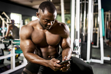 Fototapeta na wymiar African male bodybuilder blogger uses a smartphone in the gym