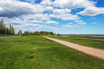 Fototapeta na wymiar spring landscape by the lake under a blue sky with clouds and running away to the forest road