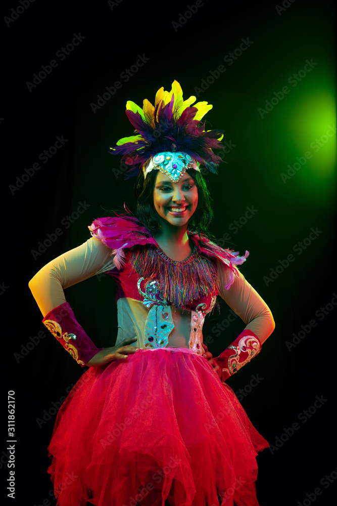 Wall mural beautiful young woman in carnival mask and stylish masquerade costume with feathers in colorful ligh