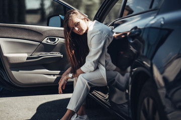 Fototapeta na wymiar Fashion Stylish Girl in White Suit Posing Near the Blue Car