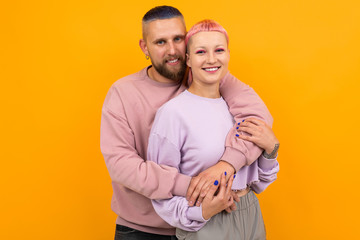 Unusual pretty woman with short pink hair and tattoo hugs with her boyfriend isolated on orange background