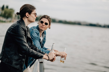 Two Stylish Twins Brothers Having Fun Drinking Beer on the Pier Near the River