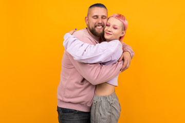Unusual pretty woman with short pink hair and tattoo hugs with her boyfriend isolated on orange...