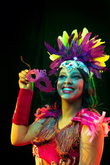 Beautiful young woman in carnival mask and stylish masquerade costume with feathers in colorful...