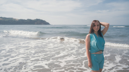 Stylish woman near waving sea. Adult female in trendy summer outfit smiling and looking at camera while standing against waving sea and cloudless blue sky on resort