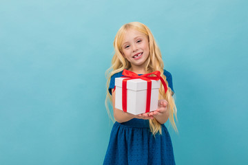 Beautiful caucasian girl holds a white box with gift and has a lot of emotions isolated on blue background
