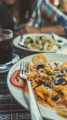 Delicious pasta with tomato sauce. Silverware placed on plate of palatable pasta with tomato sauce and olives on ornamental table in cafeteria