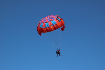 parasailing in summer with colorful parachute, two persons in blue sky