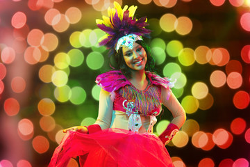 Beautiful young woman in carnival mask and stylish masquerade costume with feathers and sparklers in colorful bokeh on black background. Christmas, New Year, celebration. Festive time, dance, party.