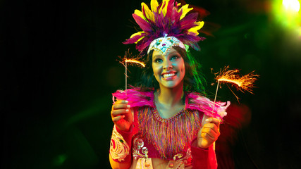 Beautiful young woman in carnival mask, stylish masquerade costume with feathers and sparklers inviting. Flyer for ad on black background. Christmas, New Year, celebration. Festive time, dance, party.