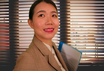 office business lifestyle portrait of beautiful and successful Asian Korean woman in executive clothes posing confident smiling cheerful at Venetian blinds window
