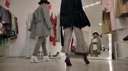 From below back view of millennial woman in black hat with brim and elegant gray suit going with consultant to mirror in fitting room, then turning round and looking at self in mirror in slow motion.