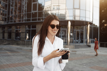 Portrait of One Fashionable Girl Dressed in Jeans and White Shirt Drinking Coffee and Using Her Smartphone, Business Lady, Woman Power Concept