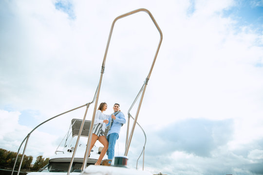Fashionable stylish standing young couple posing on luxury motorboat yacht on blue sky with clouds and sea landscape background in daylight view from the water