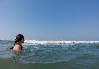 Woman waiting for sea wave. Side view of wet female swimming in sea water and waiting for foamy wave while resting on resort on sunny day