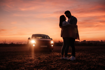 Young Happy Couple Dressed Alike in White Shirt and Jeans Enjoying Road Trip at Their New Car, Beautiful Sunset on the Field, Vacation and Travel Concept