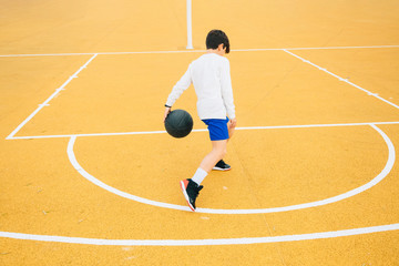 Young boy playing on yellow basketball court outdoor.