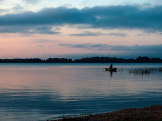 Fototapeta na wymiar evening light on the lake, fisherman in boat, dusk