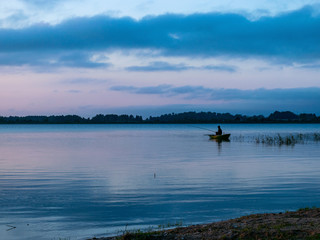 Fototapeta na wymiar evening light on the lake, fisherman in boat, dusk