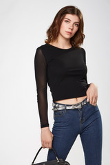 Medium full shot of a brown-haired lady in a black blouse and blue jeans with a gray leather belt...