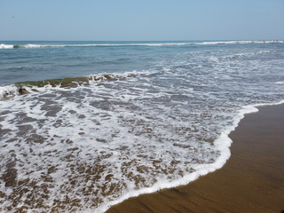 Foamy sea waves on shore. Foamy waves of clean sea water rolling on wet sandy beach on sunny day on resort
