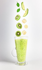 Green smoothie and falling fruits for its preparation: avocado, banana, kiwi and spinach on a neutral gray background.