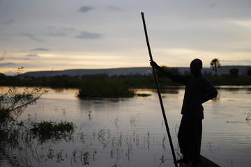 Sunset Shilouette Of An African Fisherman Standing In His Boat Holding A Push Pole