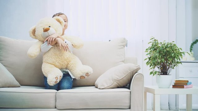 Happy little girl sitting on the sofa, hugging a big teddy-bear.