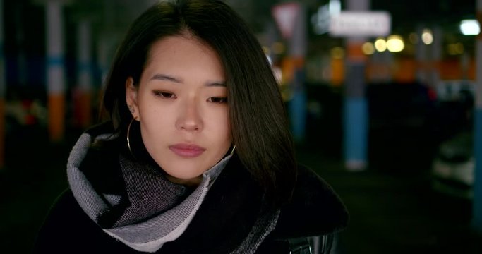 portrait of a young serious Asian woman in dark clothes and with large ring earrings in a covered Parking lot. she looks up, tucks her hair behind her ear. close up