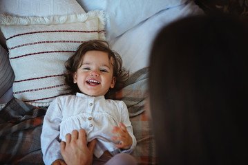 Happy loving family. Mother and her daughter child girl playing, hugging and laughing on the bed.
