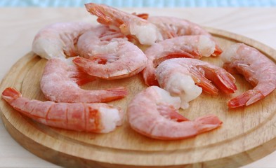 Several pieces of shrimp frozen before cooking thaw on a round board