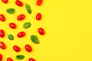 Red tomatoes and basil leaves on yellow background. Top view and copy space.