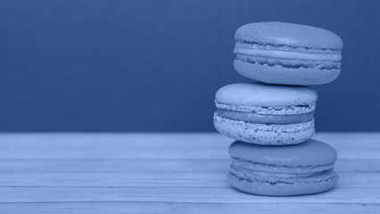 Fototapeta na wymiar Orange and blue macaroons on a dark background, French cookies as a treat for the holiday, toned trendy classic blue color of year 2020