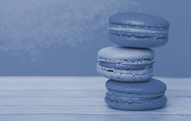 Orange and blue macaroons on yellow background, French cookies as a treat for the holiday, toned trendy classic blue color of year 2020