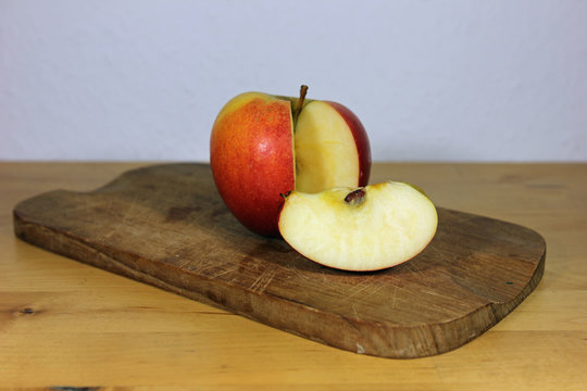 One piece cut out of an red apple on a wooden board with white background