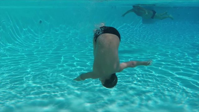 Little boy in swimming goggles dives underwater in the pool and making a double somersalts