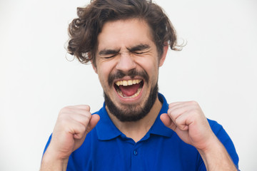 Excited overjoyed lucky guy shouting for joy, celebrating success. Handsome bearded young man in blue casual t-shirt posing isolated over white background. Winning or joy concept