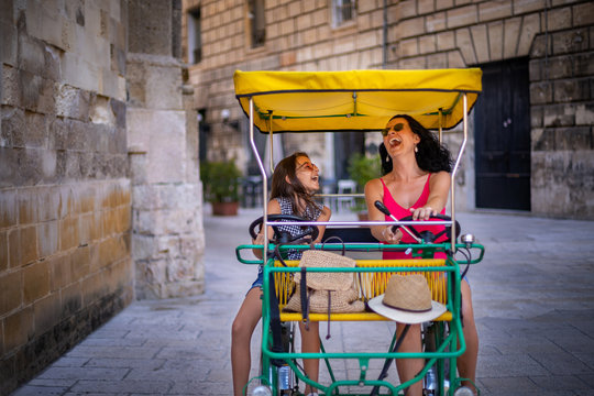 A mother and her daughter riding bicycle ( quadricycle ) at the city street of Italy