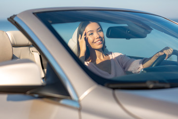 cheerful young woman sitting in the convertible and looking in the mirror